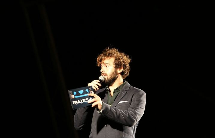Apresentador em palco com o cartão da Rialesa Produções na mão